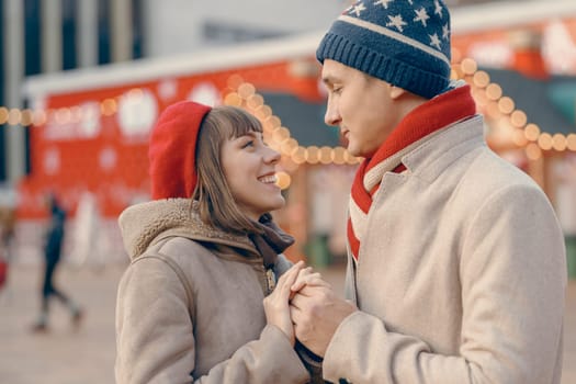 A beaming couple exchanges smiles and holds hands, with the festive glow of a Christmas market setting a romantic scene