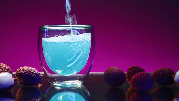 Blue drink is poured into glass on isolated background. Stock clip. Carbonated blue drink is poured into clear glass in bar. Bright drink with ingredients and fruits around.
