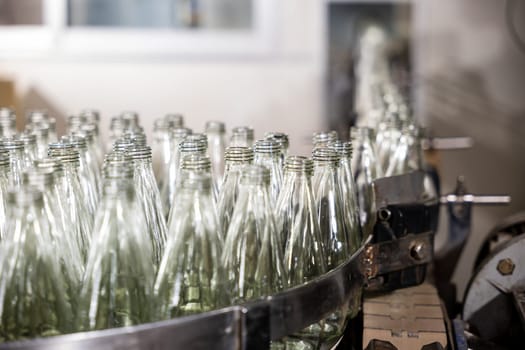 In a distillery an automated belt exhibits empty glass bottles hinting at alcoholic beverage production. The factory's modern technology promises efficient bottling procedures.