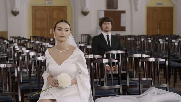 The wedding ceremony. Action.A huge hall with chairs where a young groom in a suit and a bride in a long white dress with a veil are getting married. High quality 4k footage