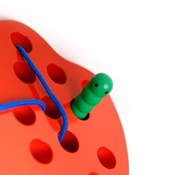 Kid's wooden toy in the shape of a red apple with a funny worm on a rope, toy for developing fine hand motor skills, copy space.