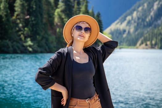 Happy woman in brown hat posing on Kolsay lake in Kolsai Koldery gorge, nature of Kazakhstan National Park in Central Asia.