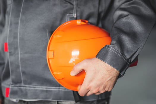 Orange safety helmet is in the hands of a construction worker, close up, construction site safety concept.