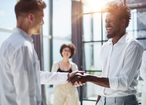 Glad to work with you. Young modern men in smart casual wear shaking hands and smiling while working in the creative office