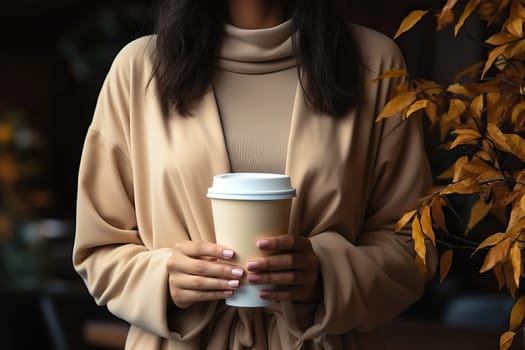 A woman holds a cup of coffee in her hands and stands on the background of a cafe, mockup for business ideas with coffee.