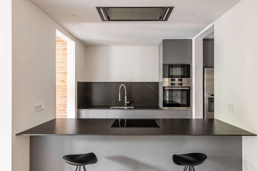 Modern kitchen with dining island and bar stools after renovation. Kitchen made from high quality design materials with built-in electrical appliances