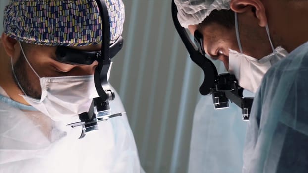 Medical team performing operation. Close up of faces of surgeons at work wearing binocular loupes in operating theatre during the procedure.