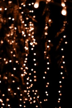 Blurry garland lights on a dark background. Festive Christmas and New Year background. Soft focus. Image toned in color of the year 2024 - Peach Fuzz.