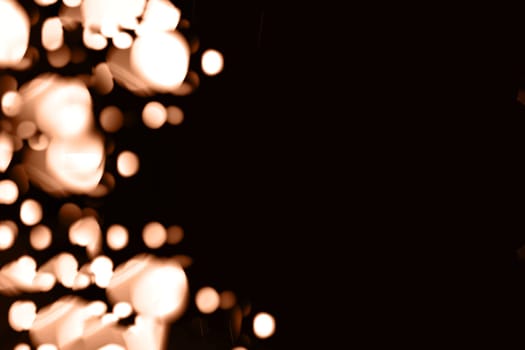 Blurry garland lights on a dark background. Festive Christmas and New Year background. Soft focus. Image toned in color of the year 2024 - Peach Fuzz.