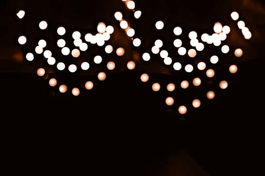 Blurry garland lights on a dark background. Festive Christmas and New Year background. Soft focus. Image toned in color of the year 2024 - Peach Fuzz.