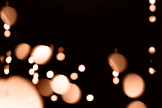 Blurry garland lights on a dark background. Festive Christmas and New Year background. Soft focus. Image toned in color of the year 2024 - Peach Fuzz.