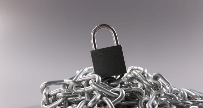 Close-up of solid metal locked padlock on top of tangled silver chain. Set to lock and protect house. Security, protection, safety concept. Copy space