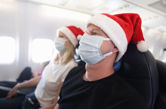 Man and woman in protective masks and santa hats flying in airplane. New year holidays during covid19 pandemic concept