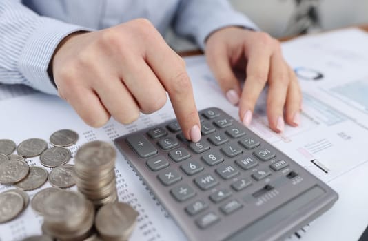 Woman counting on calculator at table with documents and coins closeup. Payment of taxes concept