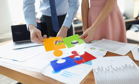 Business people folding colorful puzzle at table with documents closeup. Business cooperation concept