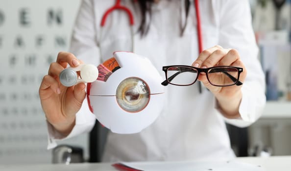 Ophthalmologist doctor holding eyeglasses and lenses near artificial model of eye closeup. Vision correction concept