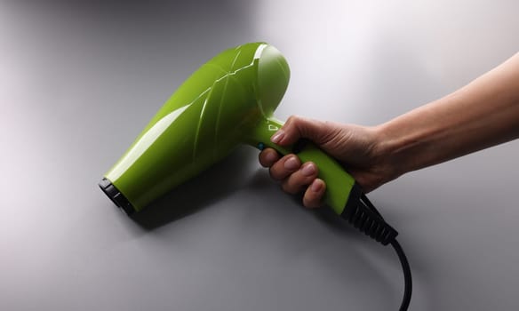 Woman holding green hair dryer in hand closeup. Hair care concept