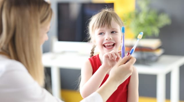 Little girl choosing toothbrush at dentists office. Daily oral care for children concept