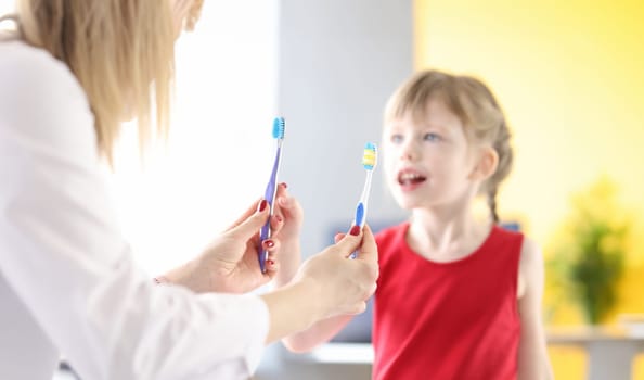 Doctor holding two toothbrushes in front of little girl. Daily brushing of teeth concept