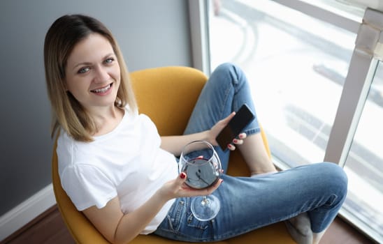 Young woman sitting on armchair with glass of red wine and phone. Self-isolation leisure concept