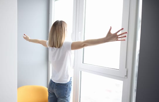 Woman spreading her arms wide and standing near window. Nice view from window concept