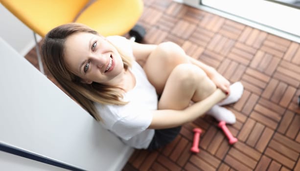 Young woman sitting on floor with pink dumbbells. Home fitness concept