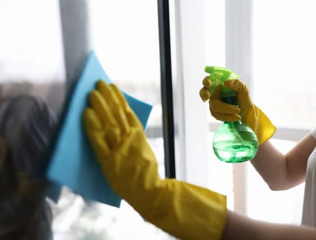 Housekeeper in gloves washing window with napkin closeup. Cleaning of apartments and offices concept