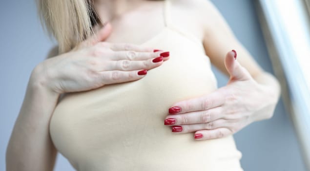 Woman palpating her breasts with hands closeup. Breast self examination concept