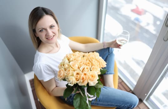 Woman with bouquet of roses sitting with glass of wine in hand. Happy birthday concept