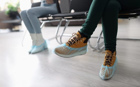 Women sitting in line with shoe covers on their feet closeup. Rules of conduct during covid19 pandemic concept