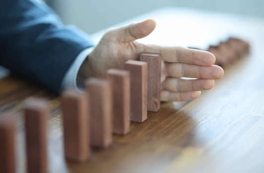 Male hand stopping falling of wooden blocks in line closeup. Financial support concept