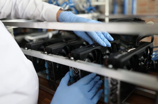 Master in gloves installing video card in mining farm closeup. Repair of computer equipment concept