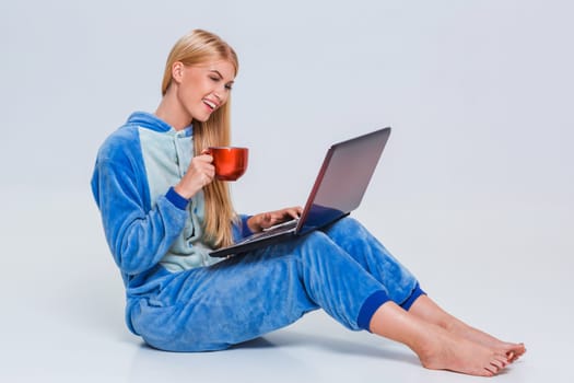 girl in pajamas with a laptop lying on the floor. studying or doing online shopping. work from home. Satisfied and smiling. drinking coffee or tea