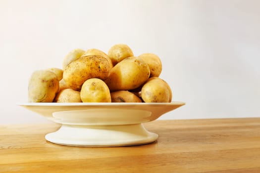 Whole yellow potatoes in plate on wooden table , uncooked and unpeeled vegetable