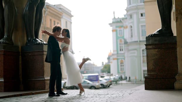 Beautiful and young just married couple posing, embracing, and holding hands outdoors. Bride and groom near giant statues