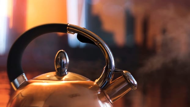 A metal silver teapot on a gas stove in the kitchen at home. Close up of steel kettle with boiling water, preparation of hot beverage.