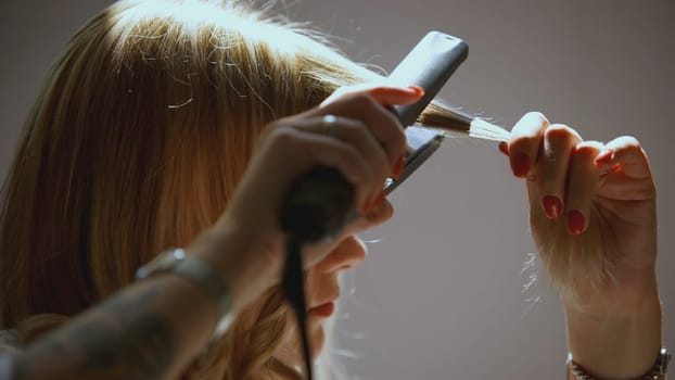 The girl winds curls on a curling iron. ART. The girl has blond hair that she curls. straightener curl hair.