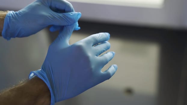 Protection against contagious disease, coronavirus, man wearing hygienic gloves to prevent infection. Close up of man hands putting on protective blue latex gloves.