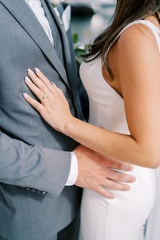 Groom hugs bride by the waist while standing on the street. Cropped. Faceless. High quality photo