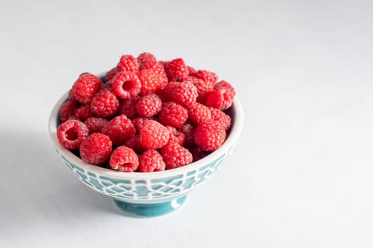 fresh raspberries in a blue bowl at the white table, summer harvest fruits and fresh berries, vitamins, vegetarian concept, High quality photo