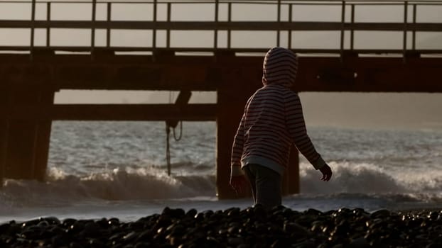 Children walking along the seashore. Creative.Little boys running along the stone beach from the waves next to buoys and bridges and you can see the sunny sky. High quality 4k footage