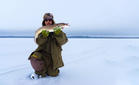 Man Holding a Fish in the Snow. Winter fishing, adventure. Banner, copy space