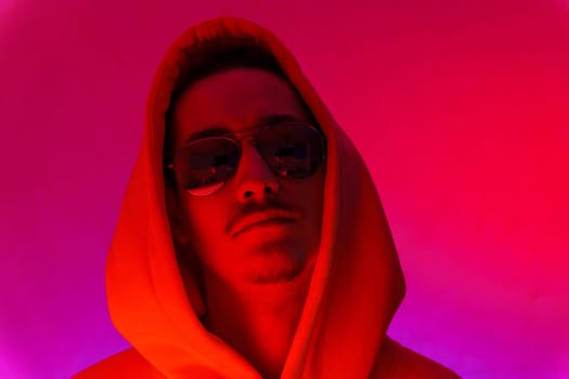 Portrait of a millennial man with glasses, red background portrait cyberstyle. Hipster in a hoodie. Selective focus