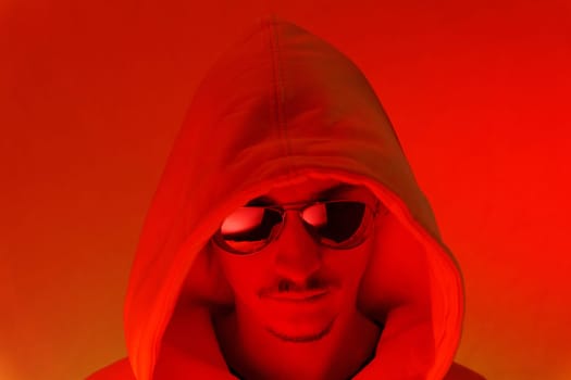 Portrait of a millennial man with glasses, red background portrait cyberstyle. Hipster in a hoodie. Selective focus