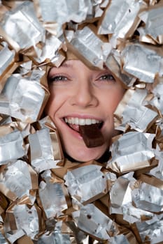 The face of a Caucasian woman surrounded by candy wrappers. The girl eats a bar of chocolate