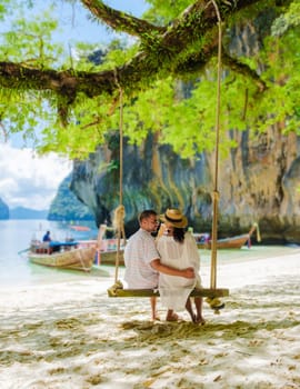 Koh Lao Lading near Koh Hong Krabi Thailand, is a beautiful beach with longtail boats, a couple of European men, and an Asian woman on the beach relaxing on a swing under a tree. Couple on a boat trip