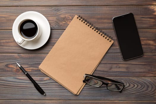 Modern office desk table with notebook, smartphone and other supplies with cup of coffee. Blank notebook page for you design. Top view, flat lay.