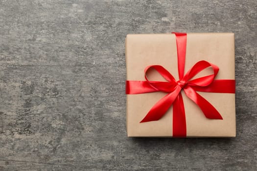 Holiday gift box wrapped in craft paper with colored bow on table background. Top view, flat lay, copy space.