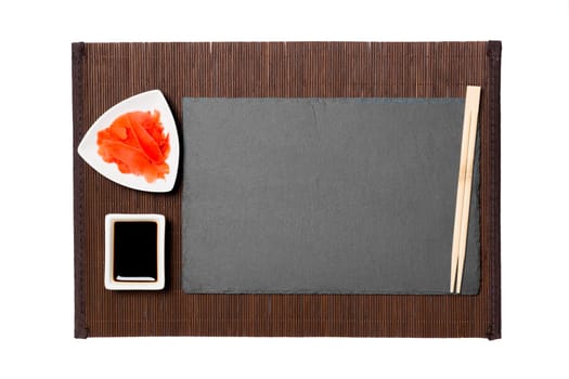 Empty rectangular black slate plate with chopsticks for sushi, ginger and soy sauce on background. Top view with copy space for you design.