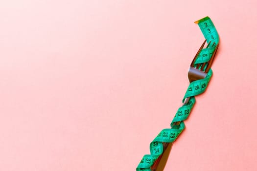 Fork wrapped in measuring tape on pink background with copy space. Top view of proper diet concept.